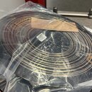 Fotografie znázorňuje smotaný kabel v černé barvě s jemnými zlatými nebo měděnými proužky, který je zabalen v průhledném plastovém sáčku. Na kabelu j…