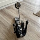 Černý basový pedál s kovovými mechanismy a řetězem. Na stupni je bílý nápis TAMA a pod ním částečně viditelný text, ze kterého je čitelné OO. Povrch…