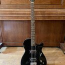 Černý elektrický basový kytara s tmavým hmatníkem. Na hlavě je zlatý nápis GRETSCH a na korpusu v pravé dolní části bílý nápis GRETSCH. Nástroj má dv…