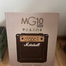 Krabice s kytarovým kompem, na které je velký nápis MG10 GOLD. Pod ním jsou ikony a texty 10 WATT, 6.5", 2 CHANNEL spolu s ikonami sluchátek a reprod…