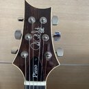 Hlava kytary z tmavého dřeva s kovovými ladičkami. Na povrchu je bílý nápis "Paul Reed Smith SE" a v dolní části nápis "Piezo". Povrch je lakovaný a…
