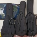Tři černé polstvuované obaly (gig bagy) na kytary, které stojí vedle sebe. Obaly mají nosní úchyty a popruhy pro přenášení na zádech. Na povrchu nejs…