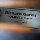 Fotografie detailu štítku uvnitř hudebního nástroje. Na bílém podkladu je černý nápis „Richard Gareis“, pod ním „OLOVi u Kraslic“ a v spodní části me…