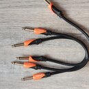 Černý rozdělovač kabelů s oranžovými plastovými kryty konektorů. Na třech z pěti viditelných konektorů je bílý nápis bespecó. Kabel má hladký povrch…