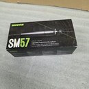Kartonová krabice s černým potiskem a zelenými detaily. Na balení je uveden název značky SHURE a model SM57, doprovázený textem Legendary Instrument…