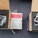 Dvě krabičky s bílými snímači značky EMG. Levý snímač má štítek s nápisy EMG-707, MADE IN USA a číslem 0116430112. Pravý snímač má štítek s nápisy EM…