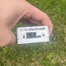 Bílé elektronické zařízení s nápisem tc electronic. Na zadní straně jsou vstupy a výstupy označené jako tuning, in, out a display. Povrch je čistý a…