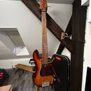 Elektrická basová kytara s trupem v červeně-žlutém sunburst provedení a tmavě červeným pickguardem. Na hlavě hmatníku není žádný viditelný nápis. V p…