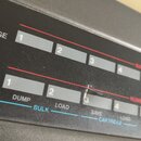Detailní záběr na ovládací panel černého elektronického zařízení. Jsou vidět dvě řady bílých obdélníkových tlačítek s čísly 1, 2, 3 a 4. Pod nimi jso…