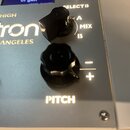 Detailní záběr na ovládací panel stříbřitého přístroje s nápisem "lotron - LOS ANGELES". Na panelu jsou umístěny dva černé oválkové knofíky a přepína…