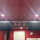 Dvě velké černé reproduktorové bedny zavěšené na kovovém hliníkovém trussu. Na přední mřížce každého reproduktoru je viditelné bílé kulaté logo s pís…