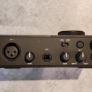 Černý kompaktní audio rozhraní s kovovým povrchem. Na zařízení jsou nápisy IN 1 u XLR konektoru, IN 2 u jackového vstupu a dvě ovratidla s popiskem G…