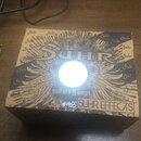 Kartonová krabice s hnědým povrchem a černým potiskem. Na horní straně je velké logo SUHR, pod kterým je nápis guitars & amps a v pravém dolním rohu…