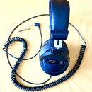 Černá uzavřená velká sluchátka s polstrováním z umělé kůže a spirálovým kabelem. Na vnější straně pravého sluchátka je nápis audio-technica, model AT…