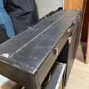 Černý obdélníkový kufýr z materiálu připomínajícího kůži s kovovými zapínacími zámky. Povrch vykazuje viditelné opotřebení ve formě zahlreichen škráb…
