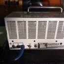 Zadní strana bílého kytarového zesilovače s kovovou rukojetí a ventilační mřížkou. Na spodním panelu jsou nápisy SPEAKER OUTPUTS, 4 OUTPUT TUBES a lo…