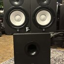 Sada tří černých studiových reproduktorů, dvě menší bedny umístěné nad jednou větší. Na spodní části každého reproduktoru je bílé logo Yamaha v kruhu…