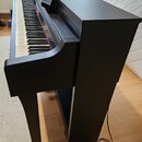 Černý digitální piano s dřevěným povrchem a integrovaným stojanem. Nástroj má standardní klaviaturu s bílými a černými klávesy a otevřený notový pult…