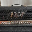 Kytarový zesilovač v černém texturovaném potahu s kovovou mřížkou, na které je nápis HOT. Na ovládacím panelu jsou kovové knofíky s popisky: INPUT, G…