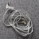 Průhledný kabel s 3,5mm jack konektorem na jednom konci a dvěma malými konektory na druhém konci. Kabel je svinutý do kroužku a položený na šedé látk…