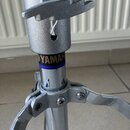 Detail stříbrného kovového stativu s nápisem YAMAHA na modrém podkladu a textem MADE IN JAPAN. Na povrchu jsou viditelné drobné škrábance a známky op…