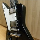 Černá elektrická kytara s bílým pickguardem a dvěma humbuckery. Na krytcích snímačů nejsou žádné viditelné nápisy ani loga. Povrch kytary je glossy,…