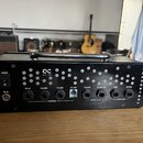 Černý oválný kontrolér s kovovou rukojetí nápisem ONECONTROL na pravém boku. Na zadní straně jsou vstupy a výstupy s popisky DELAY, CHANNEL, FX LOOP,…