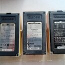 Tři černé napájecí adaptéry značky BOSS. Každý má na zadní straně štítky s technickými specifikacemi, nápisy BOSS AC ADAPTOR a informacemi o výrobci…
