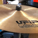 Zlatavý kovový činel s černým plastovým zpevněním v centru. Na povrchu je černý nápis UFIP Class Series EARCREATED CYMBALS. Povrch vykazuje jemné sto…