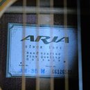 Fotografie detailu vnitřní štítku akustické kytary. Na modrém štítku je černé logo ARIA a nápisy SINCE 1956, Hand crafted Fine Quality Guitars. U Mod…