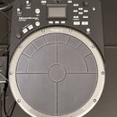 Černý elektronický perkusní pad značky Roland. Na zařízení je nápis HANDSONIC Expr/NATURAL a označení modelu HPD-20. Horní část obsahuje displej, ovl…