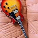 Elektrická kytara s trupem ve tvaru single-cut a barevným přechodem od červené k žluté. Nástroj má dva humbuckery s krémovými kryty, čtyři černé ovlá…