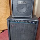 Dvě černé basové komba značky Fender, jedno umístěné na druhém. Horní menší kombo má nápisy FENDER BASS AMPLIFICATION a RUMBLE 15. Dolní větší kombo…