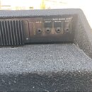 Detail zadní strany černého basového komba s chladičovými žebry. Na ovládacím panelu je nápis BA150 150W BASS AMP a čtyři vstupy s popisky AMP IN, PR…