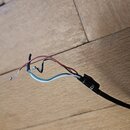 Černý elektrický kabel s odstrihlým koncem. Jsou vidět čtyři odkryté vodiče v barvách červené, černé, bílé a modré. Kabel leží na dřevěné podlaze.