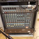 V hliníkovém racku jsou umístěna tři zařízení. V horní části je digitální reverb s nápisem REV100 DIGITAL REVERBERATOR, ve středu míchací pult YAMAHA…
