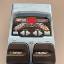 Modře stříbrný basový procesor s nápisem BP50 MODELING BASS PROCESSOR. Zařízení má červený displej, několik ovládacích tlačítek a dvě černé pedály s…