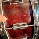 Detailní pohled na bok bubnu s tmavě červeným dřevěným povrchem a chromovanými okovů. V horní části je vidět část loga Zildjian. Povrch dřeva vykazuj…