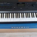 Černý digitální klavír s bílými a černými klávesami. Na levé straně horního panelu je nápis KURZWEIL a vpravo nápis Forte. Nástroj je umístěn na kart…