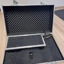 Otevřený hliníkový přepravní kufr s vnitřním polstrováním z tmavě šedé akustické pěny. V horní části víka je vložena vlnitá tlumicí pěna, zatímco dno…