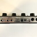 Zadní strana stříbrného efektového pedálu s четыřmi černými oválnými knoflíky. Na panelu jsou nápisy INPUT (MONO, STEREO), OUTPUT (MONO, STEREO), log…