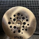 Zlatavý kovový činel s otvory různých velikostí rozmístěnými v centrální části. Ve spodní části je čitelné logo pAiste a pod ním drobný nápis MADE IN…