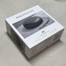 Bílá čtvercová krabice s nápisem BANG & OLUFSEN. Na horní straně je fotografie šedého kulatého reproduktoru s koženým řemínkem a text A1 2ND GENERATI…