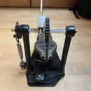 Černý basový pedál s kovovými mechanismy a řetězem. Na šlapadle je viditelný nápis "TAMA". Povrch vykazuje mírné známky používání a drobné oděrky.