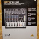 Fotografie znázorňuje krabici s míchací deskou. Na krabici je nápis XENYX X1222USB a logo behringer. Uprostřed je vyobrazen mixér s řadou potenciomet…