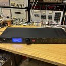 Černý rackový procesor s nápisem dbx PROFESSIONAL PRODUCTS a DriveRack PA2 SYSTEM MANAGEMENT SYSTEM. Zařízení má modrý podsvícený displej, ovládací k…