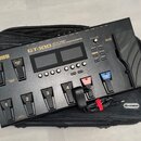 Černý kytarový procesor s nápisem BOSS a GT-100 AMP EFFECTS PROCESSOR. Zařízení má dvě displeje, několik ovládacích tlačítek a pět stupňovitých spíná…