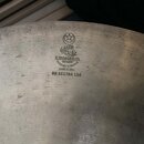 Detail povrchu kovového činele stříbrné barvy s viditelnými koncentrickými rýhami. Na povrchu je vyražen symbol hvězdy v kruhu, arabský nápis a text…