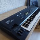Černý klavírní syntetizátor s bílými a černými klávesami. Na levé straně je bílý nápis YAMAHA MUSIC SYNTHESIZER SY99. Přístroj má ovládací panel s di…