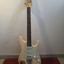 Elektrická kytara s krémovým povrchem těla a hnědým hmatníkem. Na hlavě je nápis Ibanez. Tělo má bílý pickguard, tři snímače a v dolní části jsou nal…